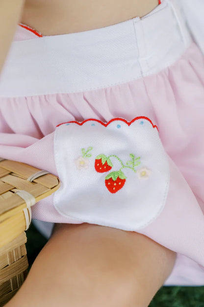 A pink baby bubble romper with white trim and strawberry appliques on the pockets and a ruffled collar.