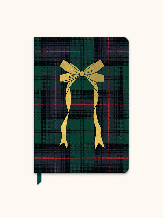 A hardcover notebook featuring a dark green and black tartan plaid pattern with thin red lines, decorated with a large golden-yellow ribbon bow graphic in the center, and a dark green ribbon bookmark hanging from the bottom edge.