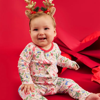 Baby wearing a floral onesie and reindeer antlers on a red background