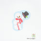 Cross-stitched snowman with a carrot nose, black hat, and red scarf on a white background.