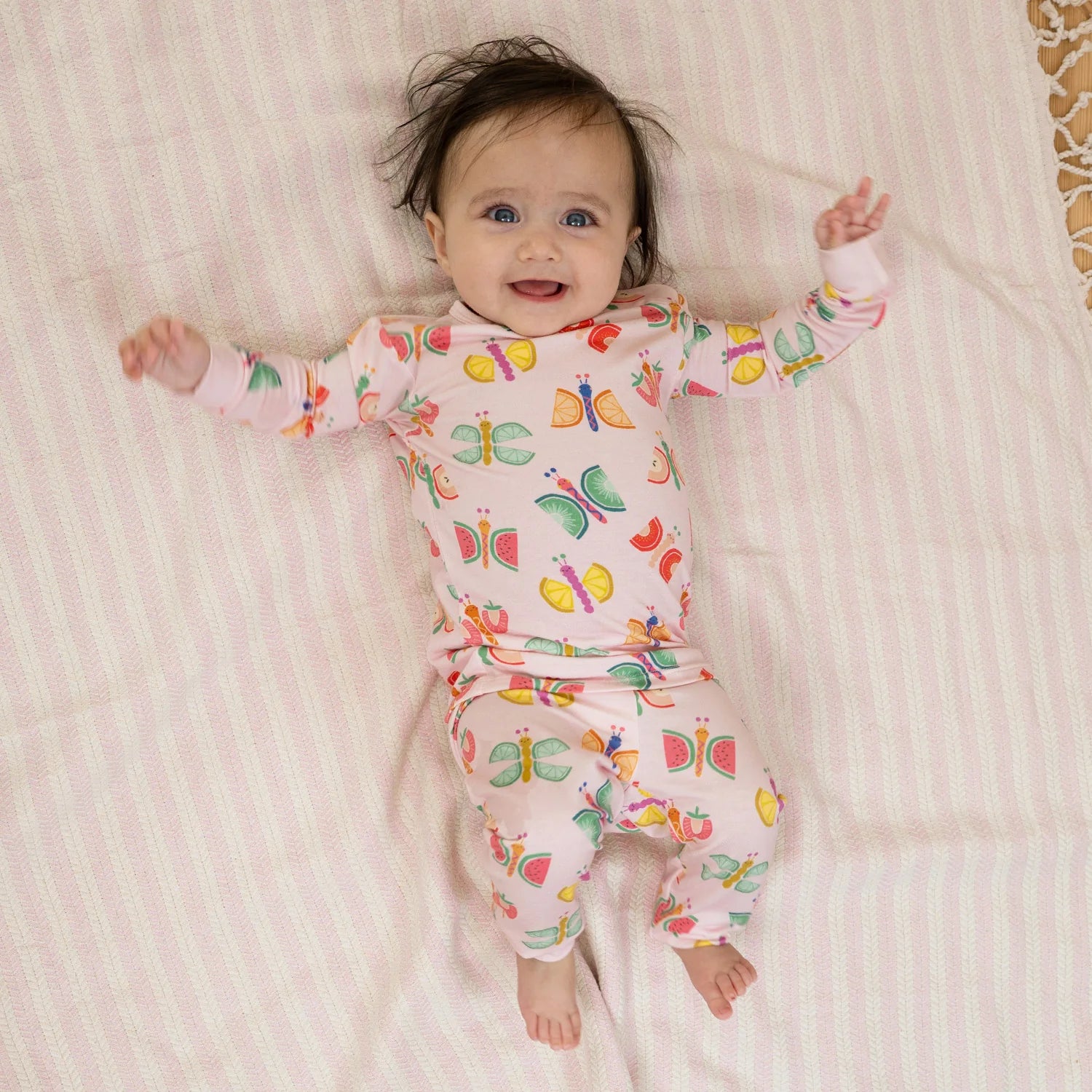 Baby wearing a colorful butterfly-patterned onesie on a striped blanket