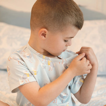 Child wearing a light blue shirt with a pattern, sitting on a sandy beach.
