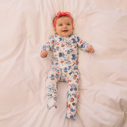 Baby wearing a colorful onesie with vehicle patterns on a soft pink blanket