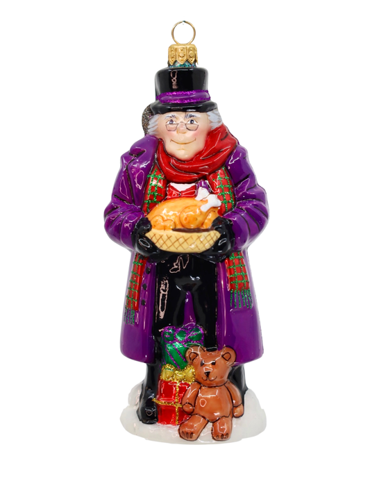 A festive Christmas ornament depicting a happy Ebenezer Scrooge in a purple coat and top hat holding a roasted turkey, with a small brown teddy bear and wrapped gifts at his feet, on a white background.
