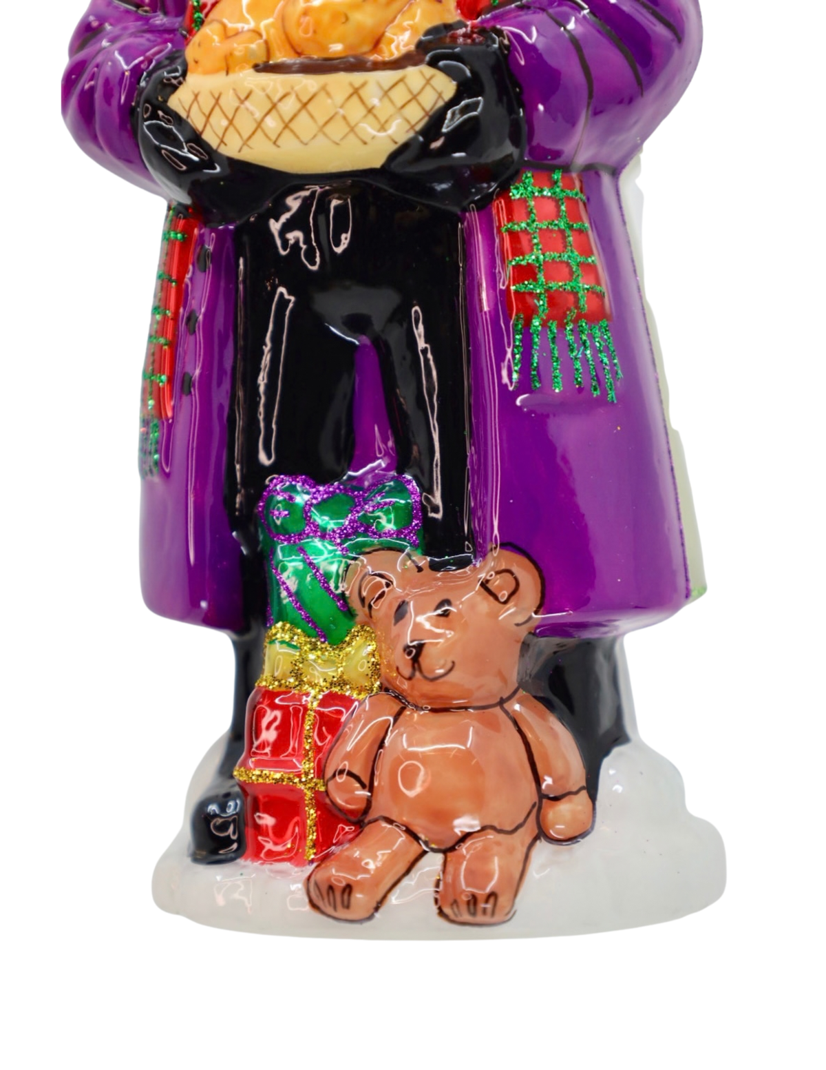 A colorful ceramic figurine of a person in a purple coat holding a basket of fruit, standing next to a brown teddy bear and wrapped gifts on a white base.