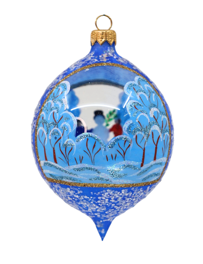 A blue Christmas ornament with a hand-painted winter landscape scene, featuring snow-covered trees, a snowy hill, and a small couple under a starry night sky. The ornament has gold glitter trim and a gold hanging loop at the top.