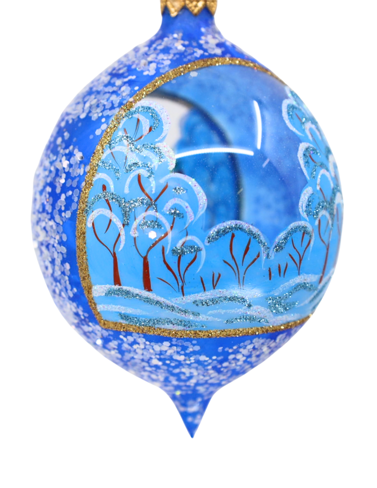 A blue Christmas ornament with a hand-painted winter forest scene, featuring snow-covered trees, a blue sky, and gold glitter accents.