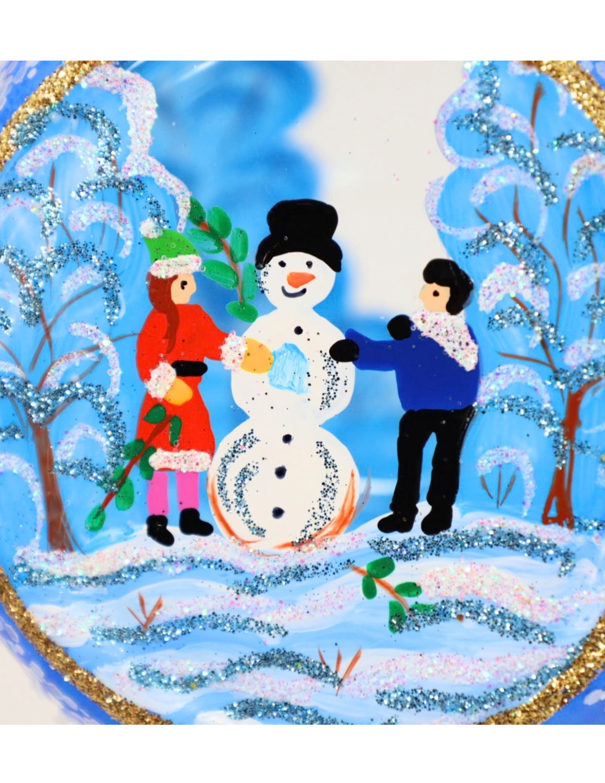 A festive circular decorative plate or plaque featuring a hand-painted winter scene with a snowman, a child in a red coat, and another child in a blue sweater, surrounded by snowy trees and a gold glitter border.