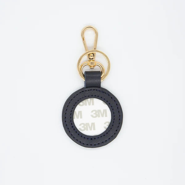 A black circular leather keychain tag with a gold-tone metal clasp and key ring, featuring a visible 3M adhesive backing on the inside of the ring, shot against a plain white background.