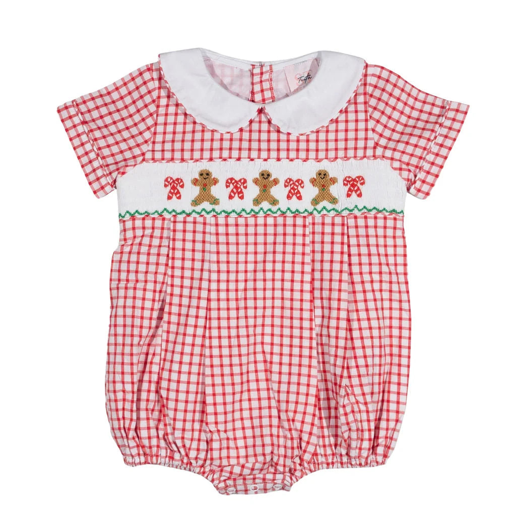 A baby romper in a red and white gingham pattern, featuring a white Peter Pan collar, a smocked chest band with embroidered gingerbread men and candy canes, and a green zigzag border.