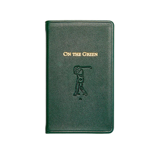 A dark green textured leather golf notebook with gold foil lettering reading 'ON THE GREEN' and an embossed golfer silhouette on the front cover, shown against a plain white background.