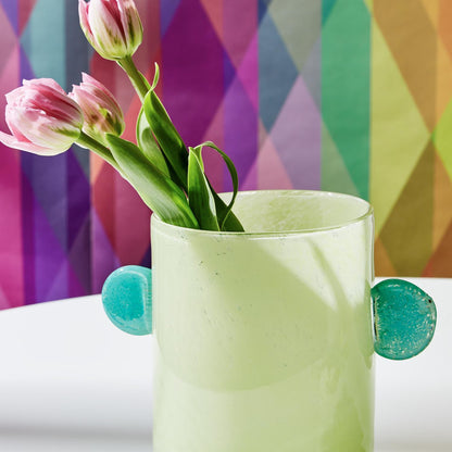 green vase with a tulip sicking out of it. colorful background