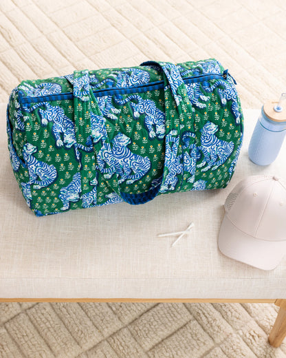 Green duffel bag with blue tiger pattern on a light wooden floor.