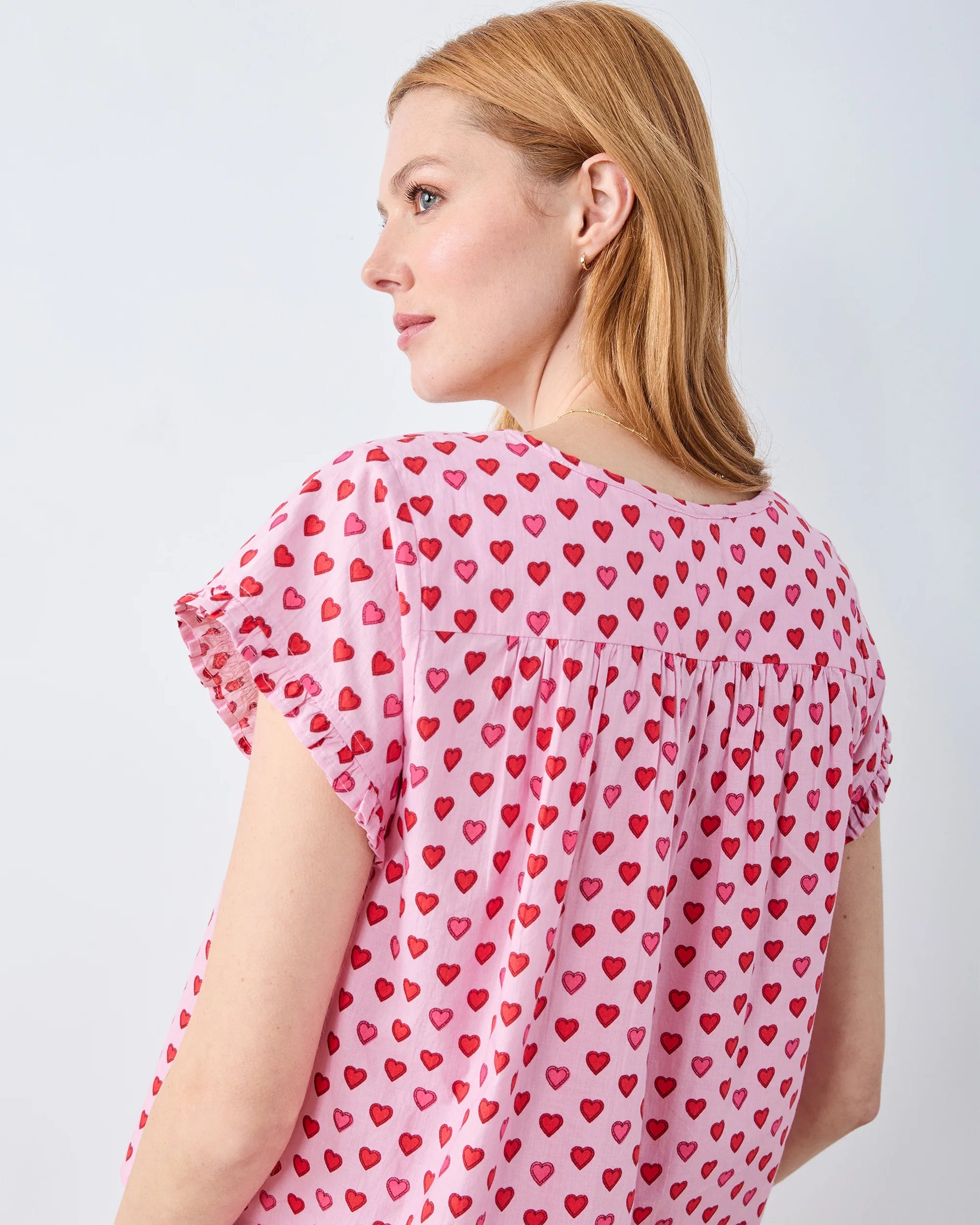 Woman wearing a pink blouse with red heart patterns on a light gray background