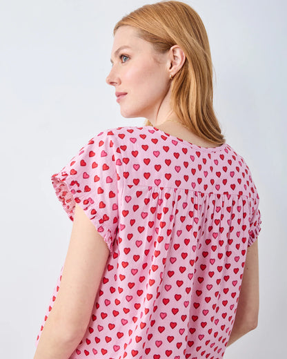 Woman wearing a pink blouse with red heart patterns on a light gray background