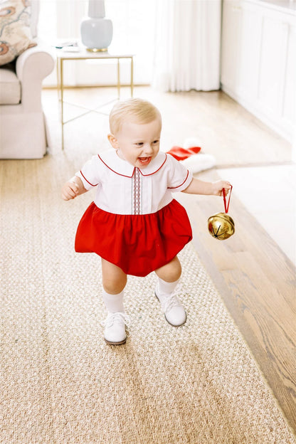 Child in a red and white outfit holding a gold bell in a living room.