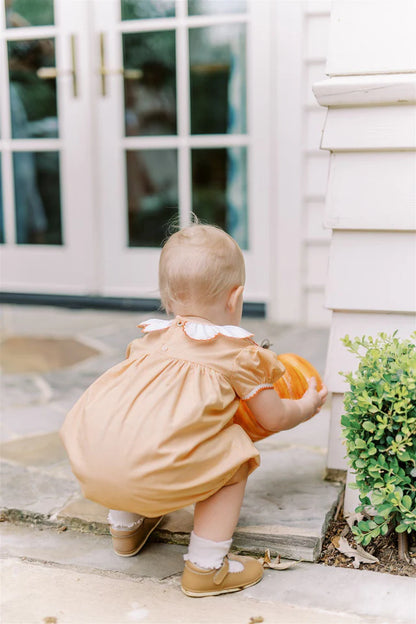 Child in a yellow dress holding a small pumpkin outside a house.