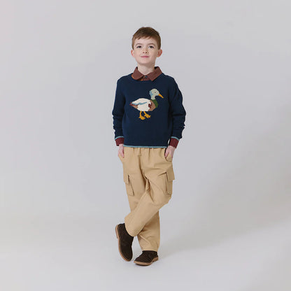 Child wearing a navy sweater with a duck design, beige pants, and brown shoes on a white background