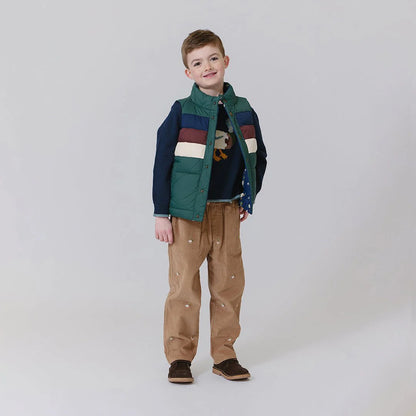 Child wearing a colorful jacket and brown pants on a plain background