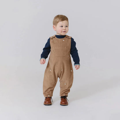 Child wearing brown overalls and a navy shirt on a plain background