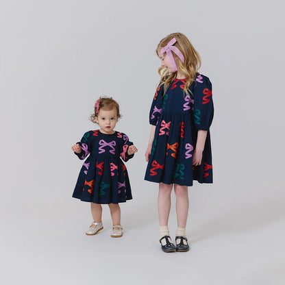 Two children wearing matching navy dresses with colorful patterns on a white background