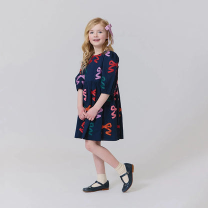 Young girl wearing a navy dress with colorful patterns on a white background