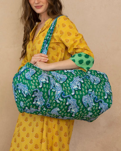 Woman holding a green and blue patterned bag against a beige background