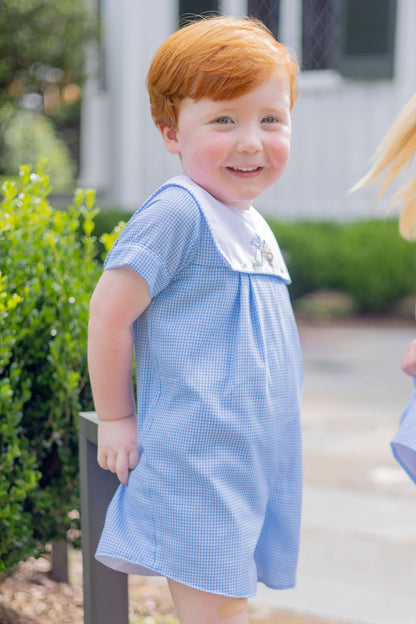 Child wearing a blue checkered dress with a white collar outdoors.