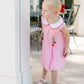 Young girl in a pink dress with cherry details standing outdoors.