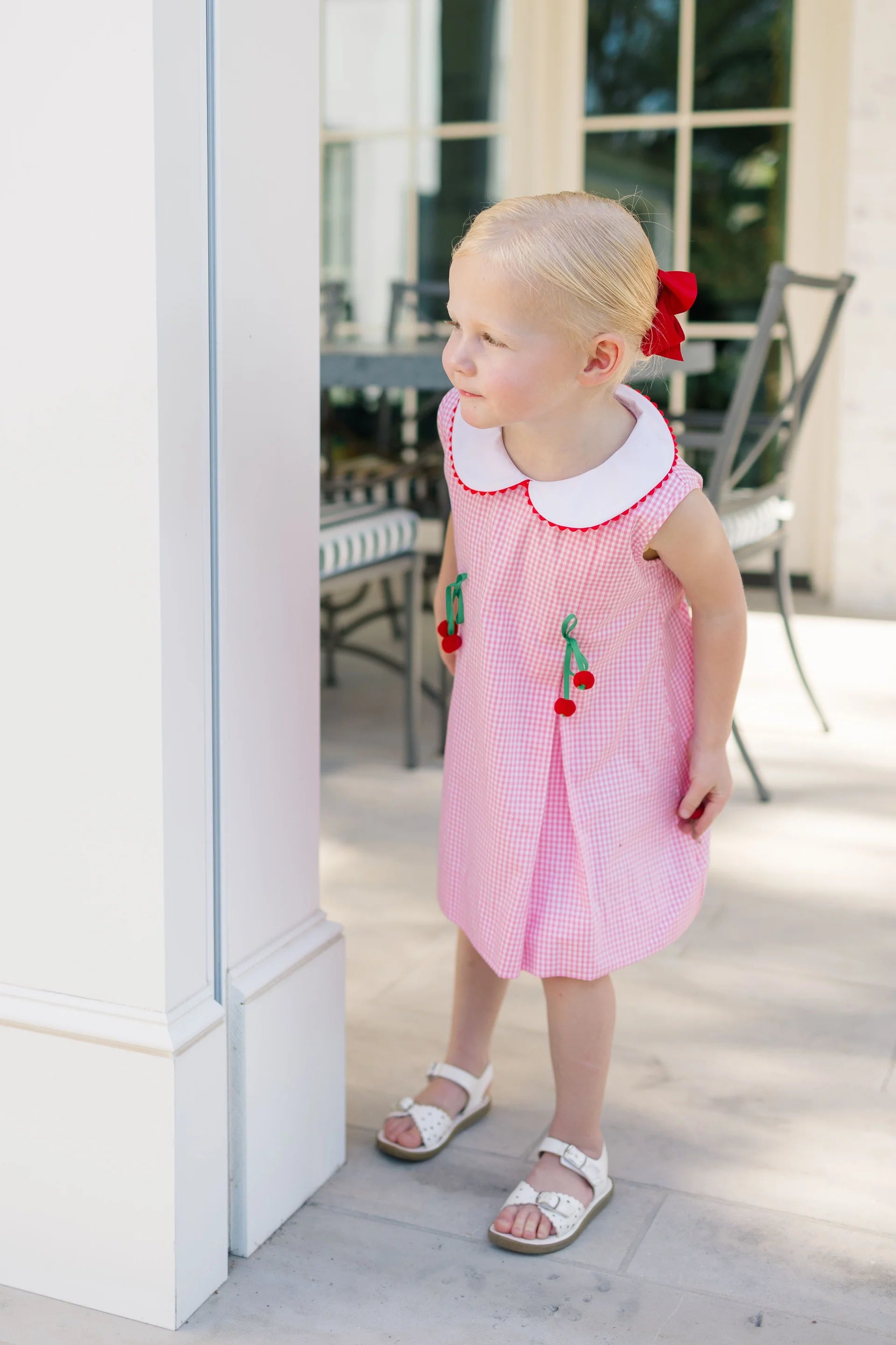 Young girl in a pink dress with cherry details standing outdoors.