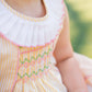 Close-up of a child wearing a white dress with colorful embroidery, blurred green background