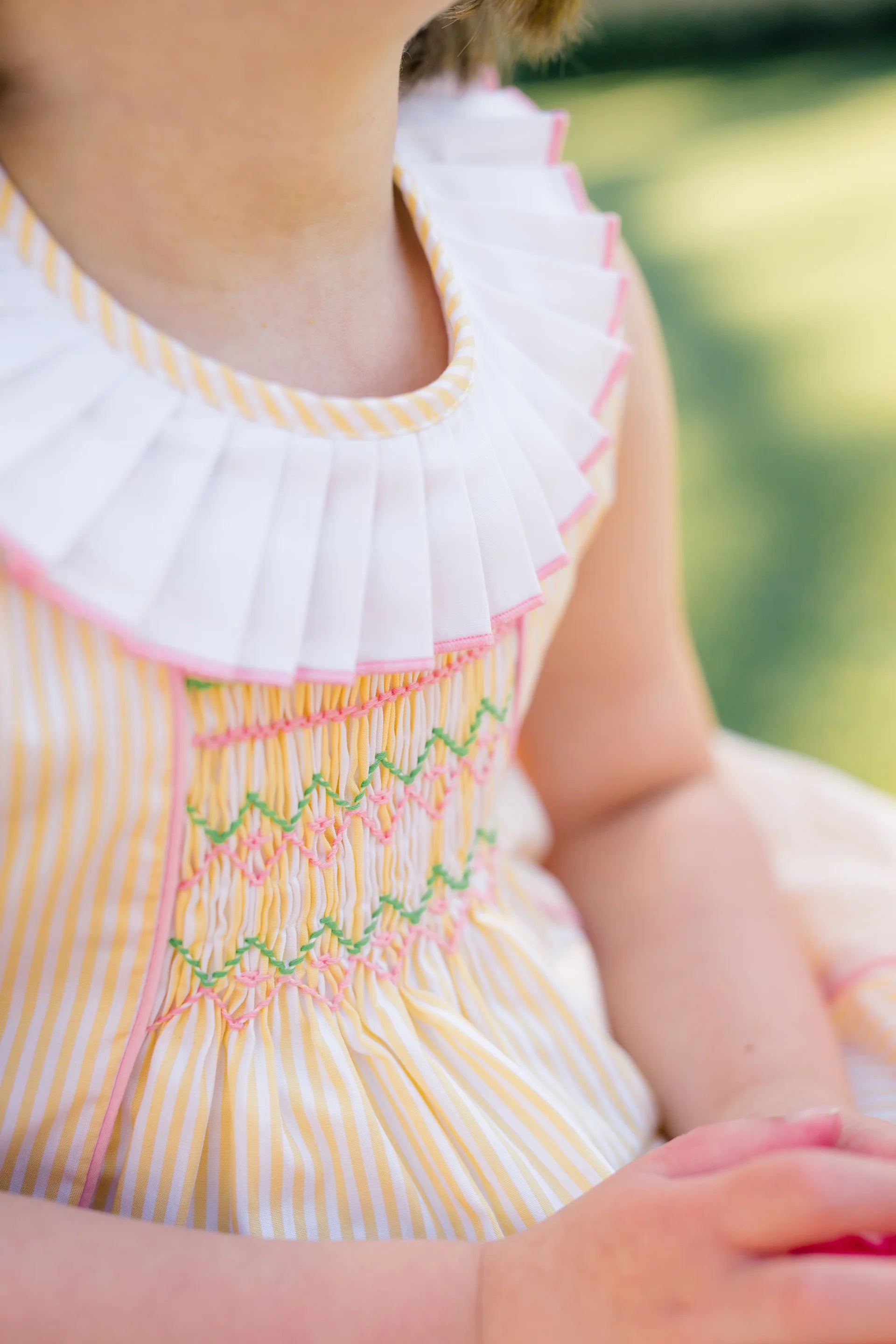 Close-up of a child wearing a white dress with colorful embroidery, blurred green background