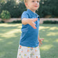 Child wearing a blue shirt and yellow rain boots standing on grass