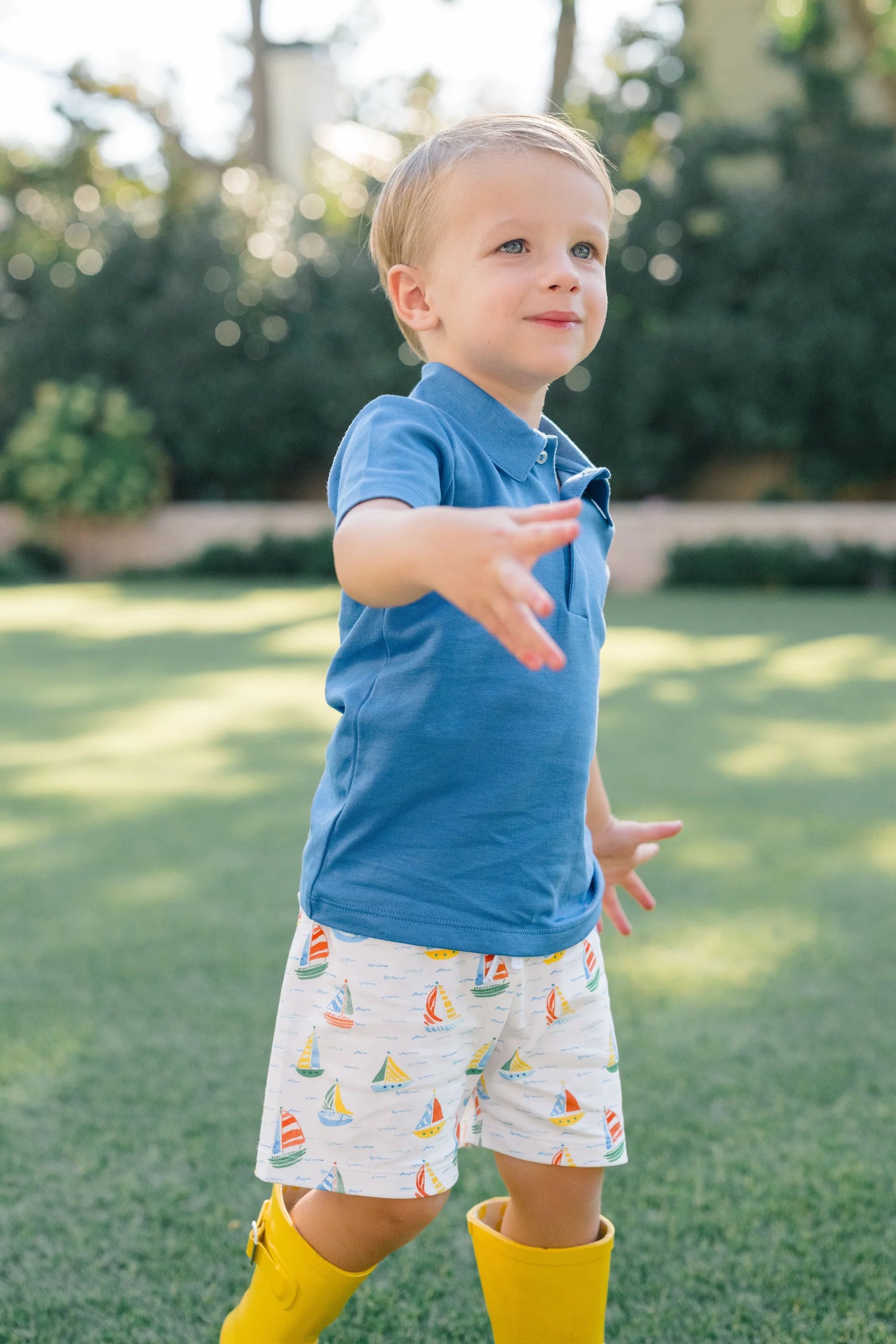 Child wearing a blue shirt and yellow rain boots standing on grass