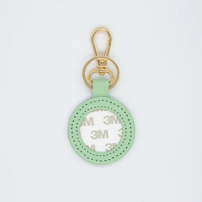 A mint green leather keychain or bag charm with a gold-tone swivel clasp and a circular cutout showing a white 3M adhesive backing, set against a plain white background.