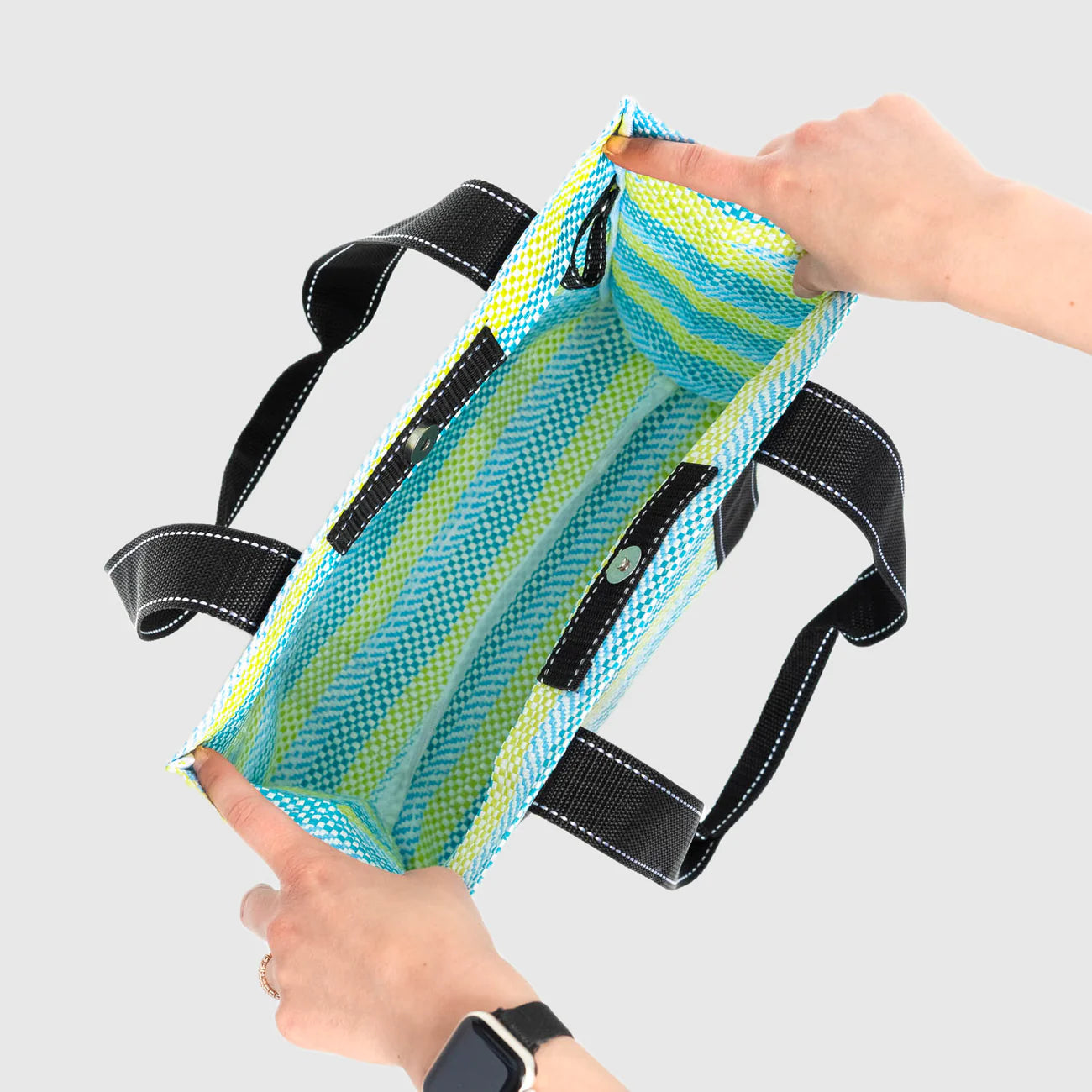 Mesh bag with black straps held by a person against a light gray background