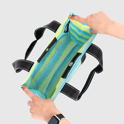 Mesh bag with black straps held by a person against a light gray background