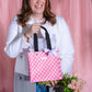 Person holding a pink patterned bag with a black strap against a pink background