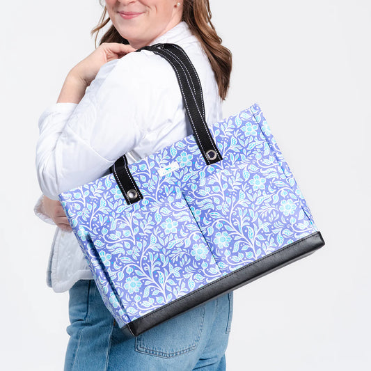 Person holding a blue floral-patterned tote bag with black accents.