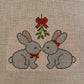 Two gray rabbits with red bows and a holly berry tree on a cross-stitched background