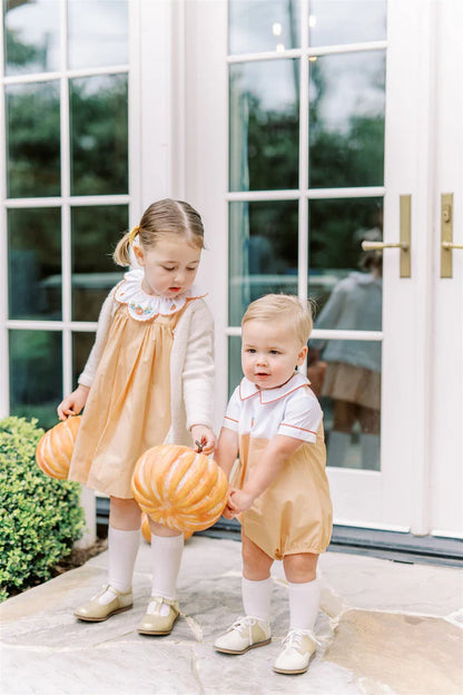 Two children in matching outfits holding pumpkins in front of a glass door.