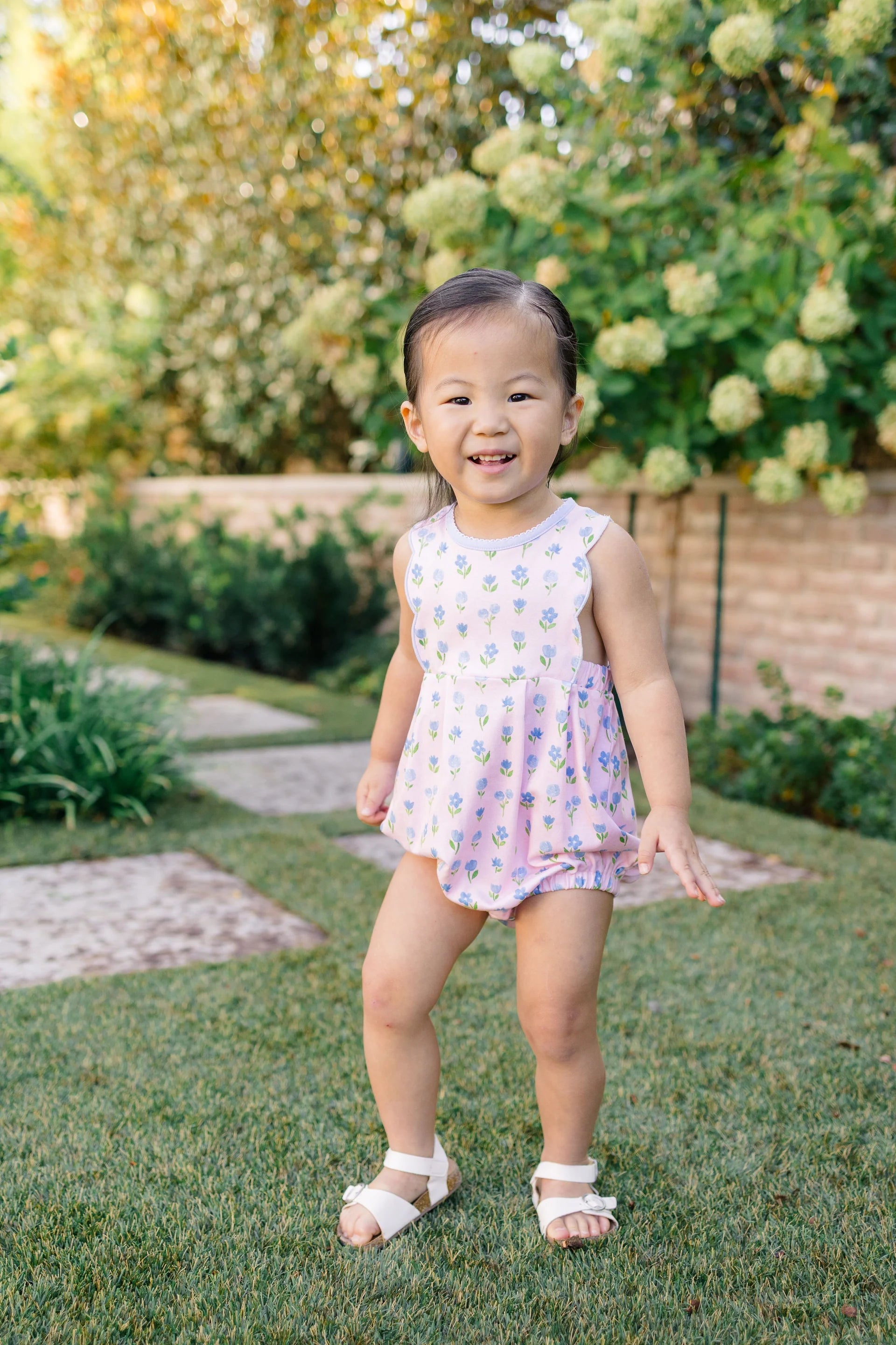 Young child in a floral dress standing on grass with trees in the background