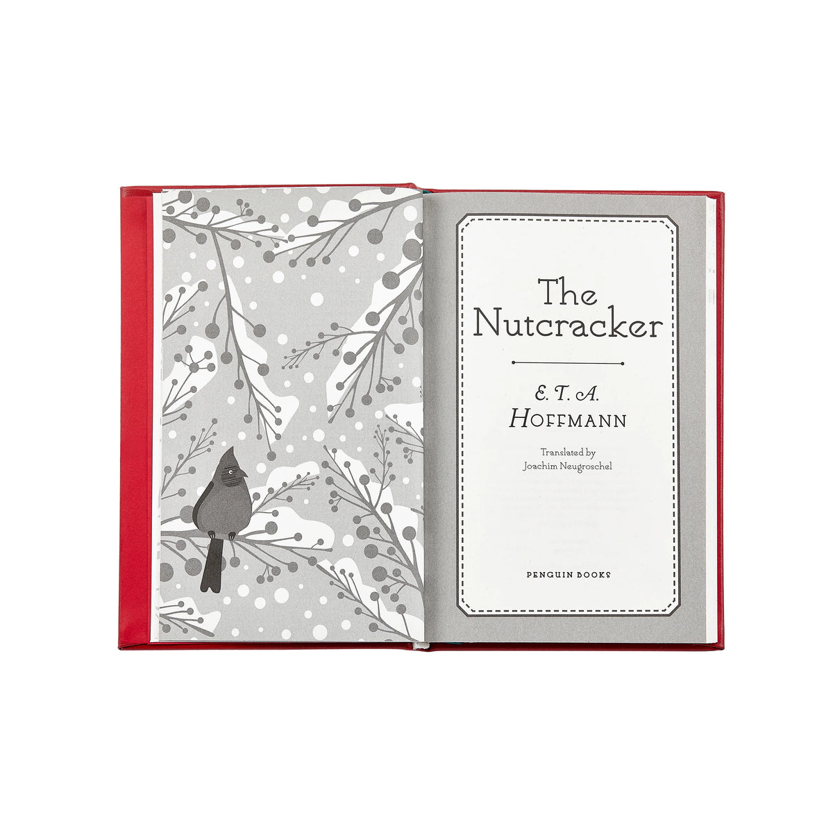 An open hardcover book with a red cover and gray-and-white illustrated interior pages. The left page shows a bird perched among winter branches, and the right page displays the title 'The Nutcracker & T.