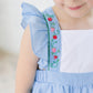 Close-up of a child wearing a blue checkered dress with floral embroidery on a white background
