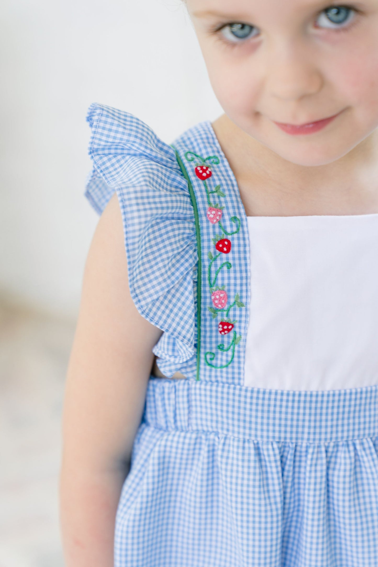 Close-up of a child wearing a blue checkered dress with floral embroidery on a white background