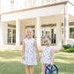 Two young girls in matching dresses standing in front of a large house.