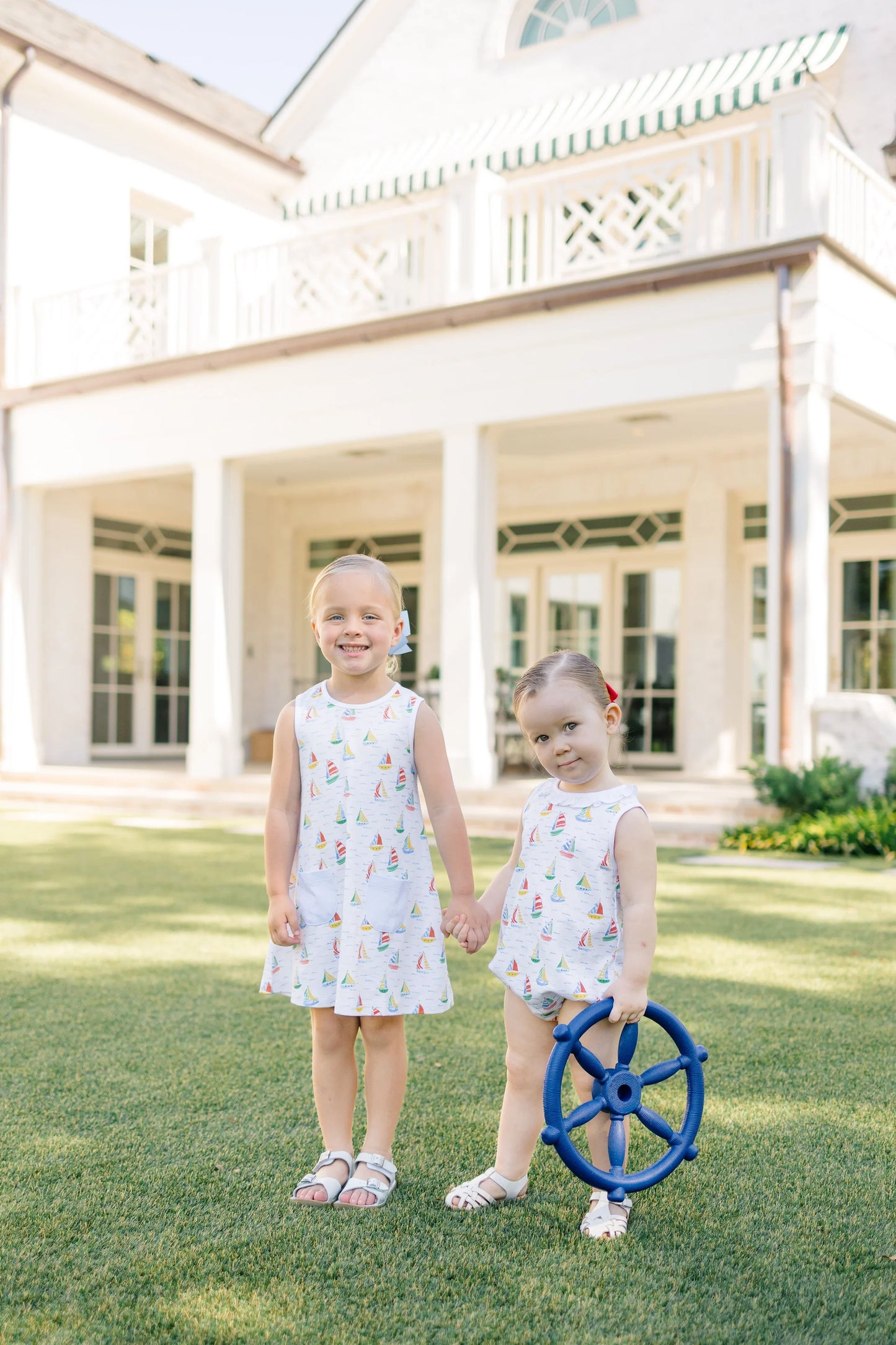 Two young girls in matching dresses standing in front of a large house.