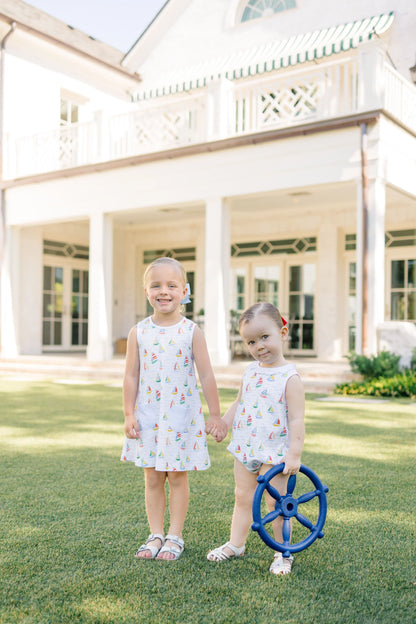 Two young girls in matching dresses standing in front of a large house.