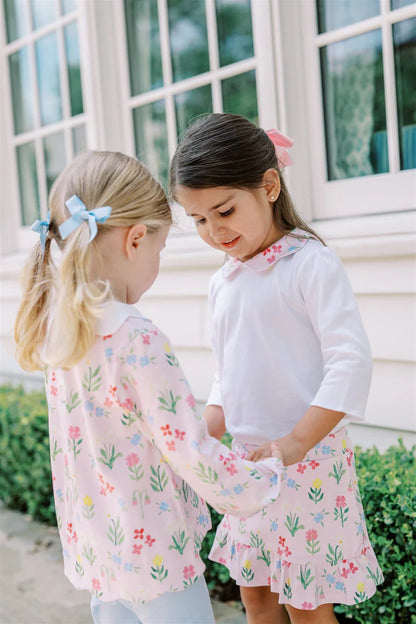 Two young girls in matching floral outfits standing outdoors.