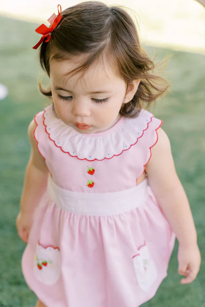 A pink baby bubble romper with white trim and strawberry appliques on the pockets and a ruffled collar.
